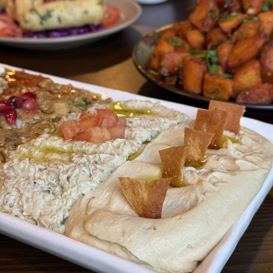 A white platter with two Mediterranean dips, one topped with tomatoes and the other with pita chips.