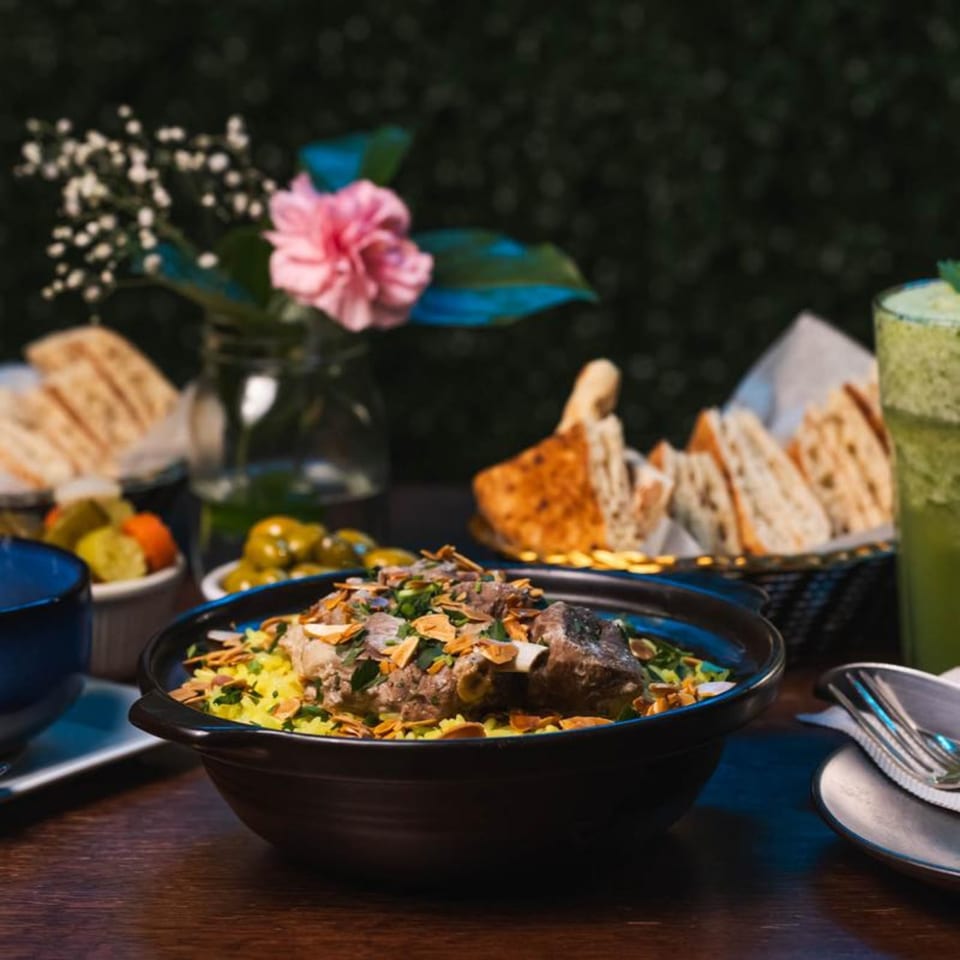 Mediterranean lamb and rice dish with almonds, parsley, bread, olives, and a green drink.