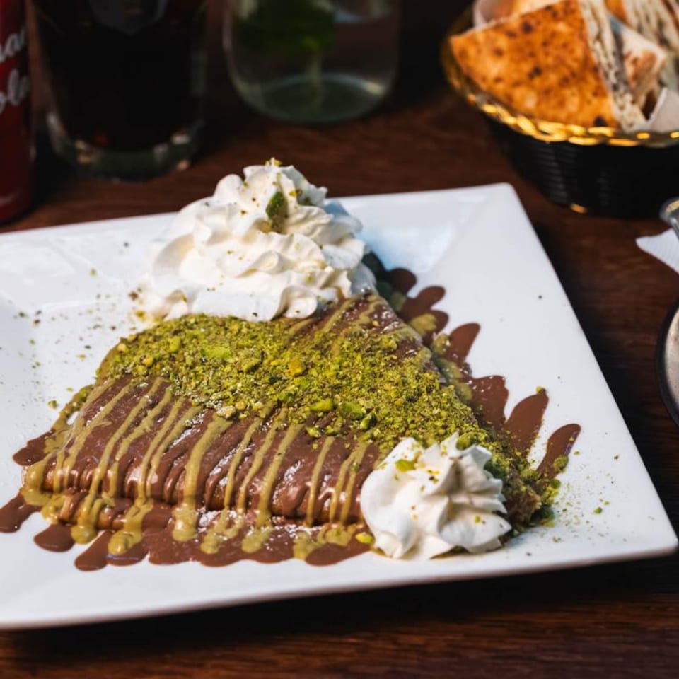 A chocolate and pistachio crepe with whipped cream on a white rectangular plate at Charcoal Gardenia.