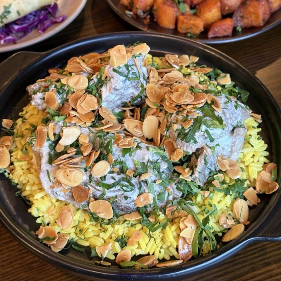 A Mediterranean dish with yellow rice, meat in a creamy sauce, fresh herbs, and sliced almonds.