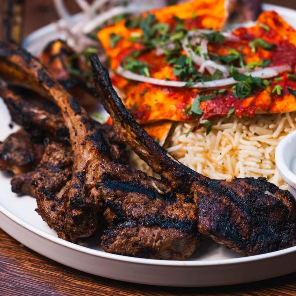 Charcoal Gardenia's grilled lamb chops, rice, and flatbread with red sauce and herbs on a white plate.