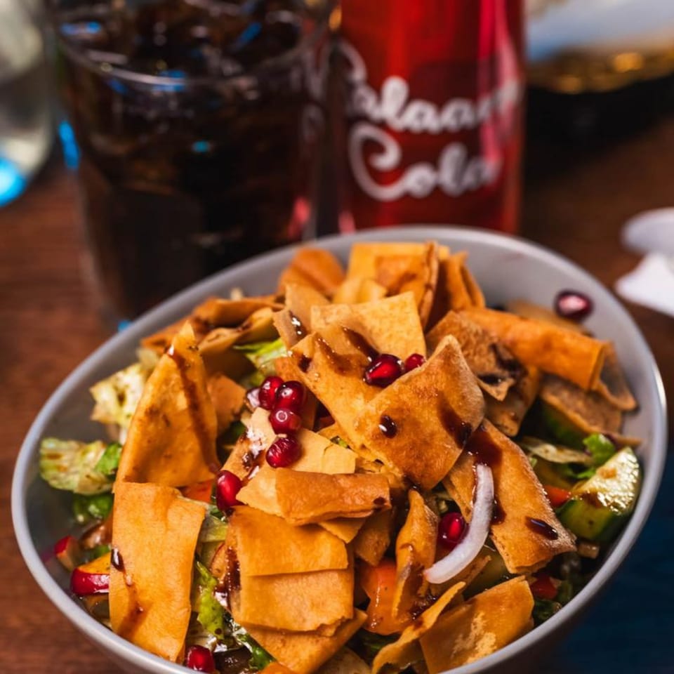 A vibrant Mediterranean fattoush salad with pomegranate, crispy pita, and a dark drink.