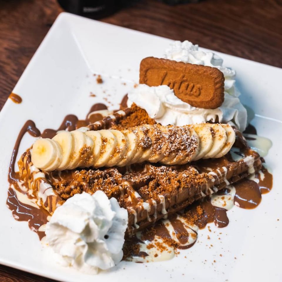 Waffle with sliced bananas, whipped cream, chocolate drizzle, and a Lotus Biscoff cookie.