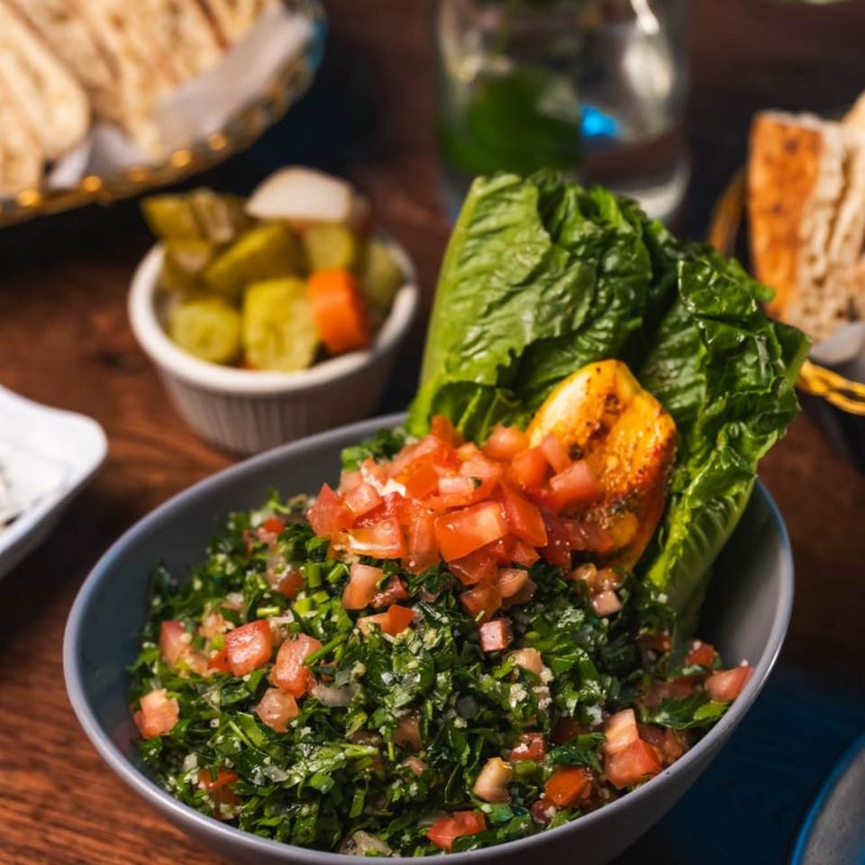 A vibrant Mediterranean tabbouleh salad with fresh tomatoes, parsley, and lettuce, served with pickles.